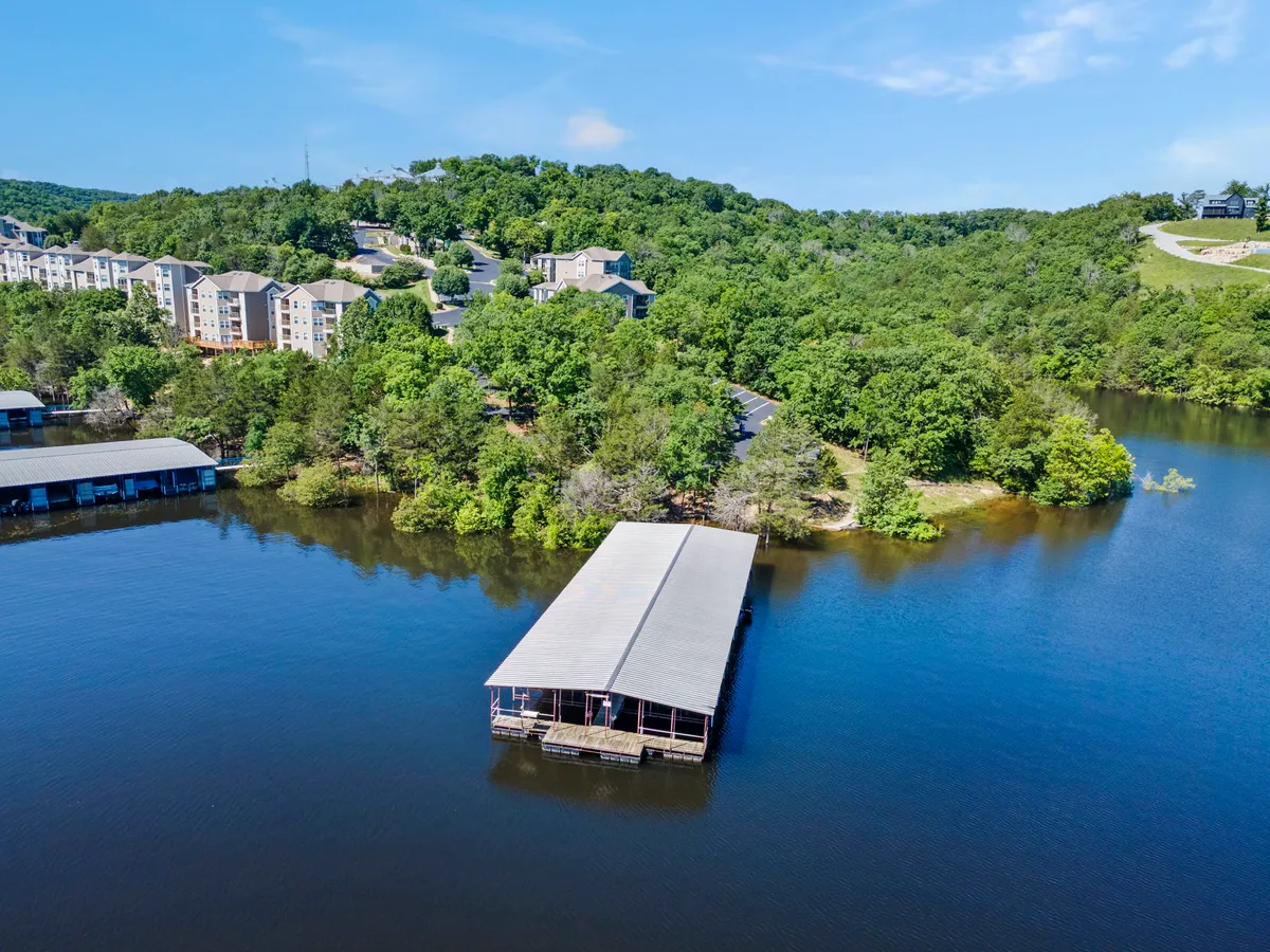 The image captures a tranquil dock stretching over calm water, surrounded by lush woods and neighboring retreat buildings. The peaceful scene invites contemplation and romantic strolls along the lakeside, with the promise of sunsets and quiet moments.