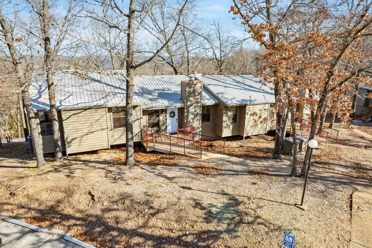 The image showcases the welcoming front entrance of Ridgeline Retreat framed by lush trees and a charming stone chimney, creating a serene and inviting atmosphere. The porch area hints at a peaceful space to relax and enjoy the natural surroundings, perfect for morning coffee or evening conversation.