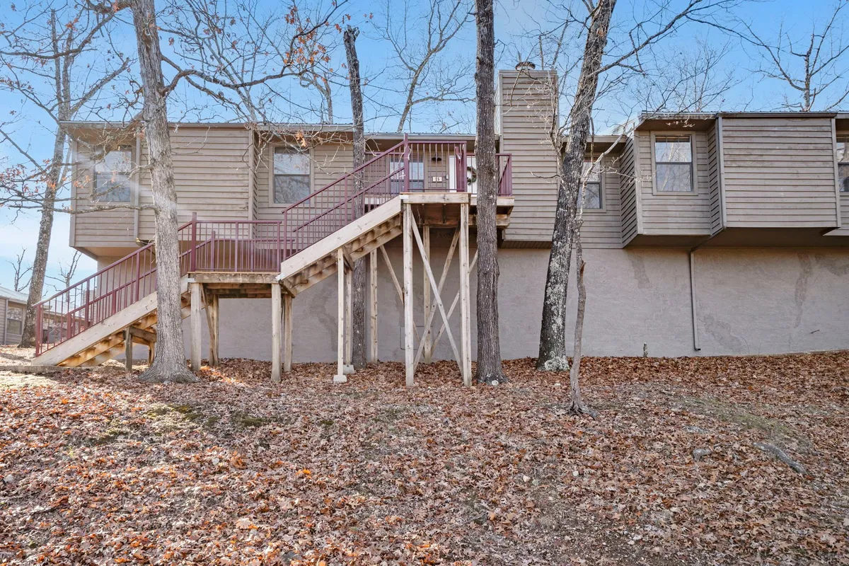 This image displays a wooden staircase surrounded by trees and a leaf-strewn ground, evoking a sense of natural tranquility. The exterior siding of the building is visible, suggesting immediate access to nature and nearby walking trails.
