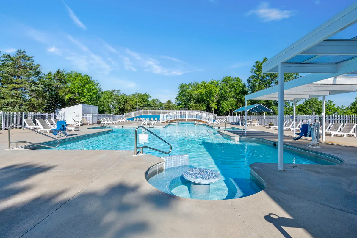 A lively outdoor pool area surrounded by lush greenery, featuring a sparkling swimming pool, a relaxing hot tub, and several lounge chairs arranged for sunbathing and socializing. The scene conveys a sense of relaxation, with children playing in the water and families enjoying the poolside atmosphere.
