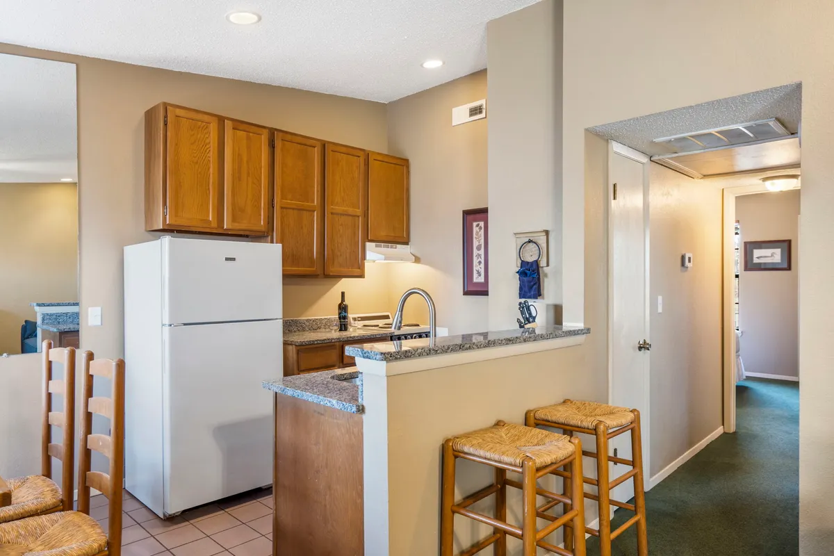 A bright, welcoming kitchen featuring modern cabinetry, expansive countertops, bar stools for casual dining, and visible appliances that suggest a fully equipped environment. Plenty of workspace and comfortable seating invite both meal prep and relaxed conversation.