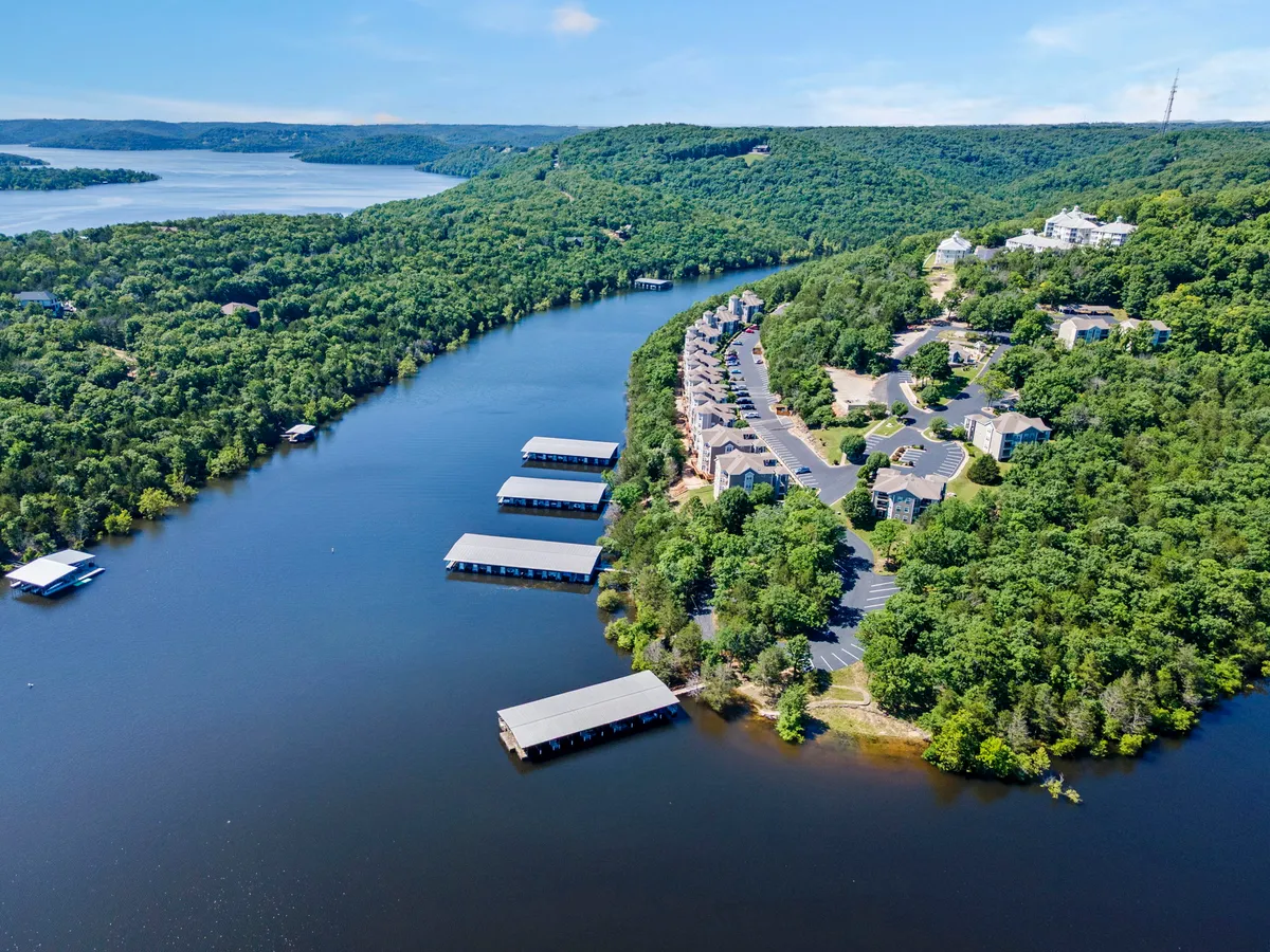 A scenic view of the lakeside resort community, including well-kept boat docks, lush greenery, river bends, and homes nestled along the water. The ambiance is peaceful, with opportunities for boating, fishing, and waterfront relaxation clearly visible.