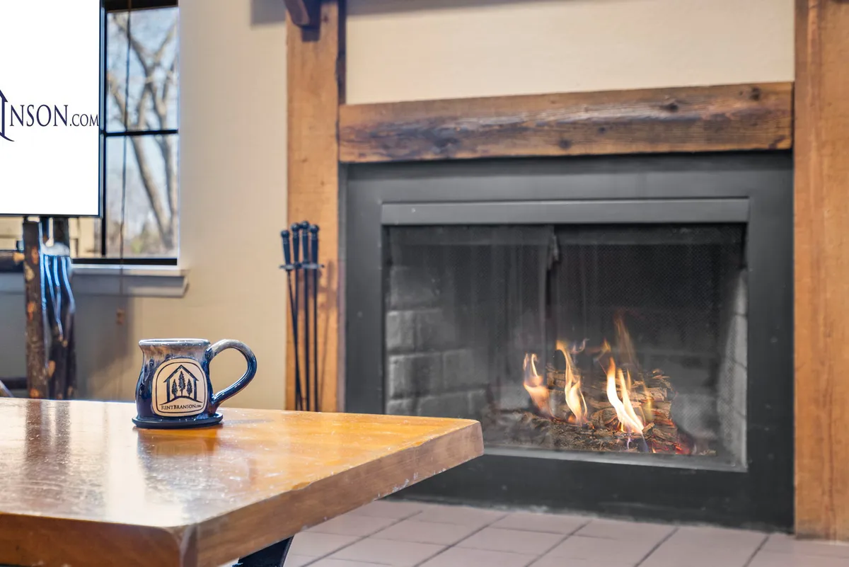 A close-up of the fireplace area with a wooden table set with a coffee mug. The soft glow from the fireplace adds warmth to the space, creating an intimate spot for reading, sipping a drink, or enjoying a quiet moment.