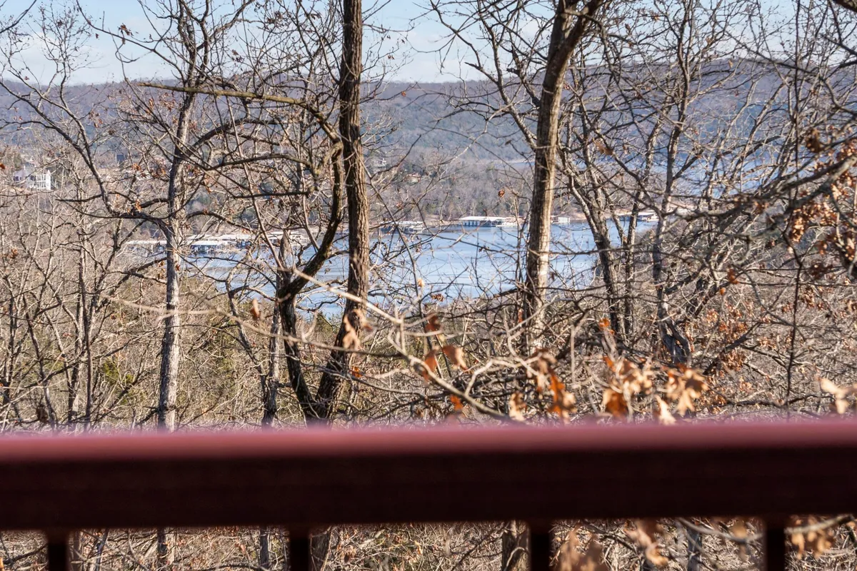 A peaceful panoramic view of the lake, surrounded by trees and distant rolling hills. The vantage suggests the experience of hiking or relaxing on a deck, with the natural beauty of sunrise or sunset highlighting the landscape.